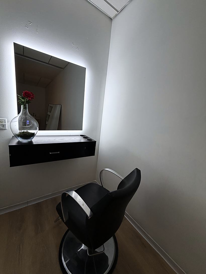 A styling station with a backlit mirror, floating black cabinet and styling chair
