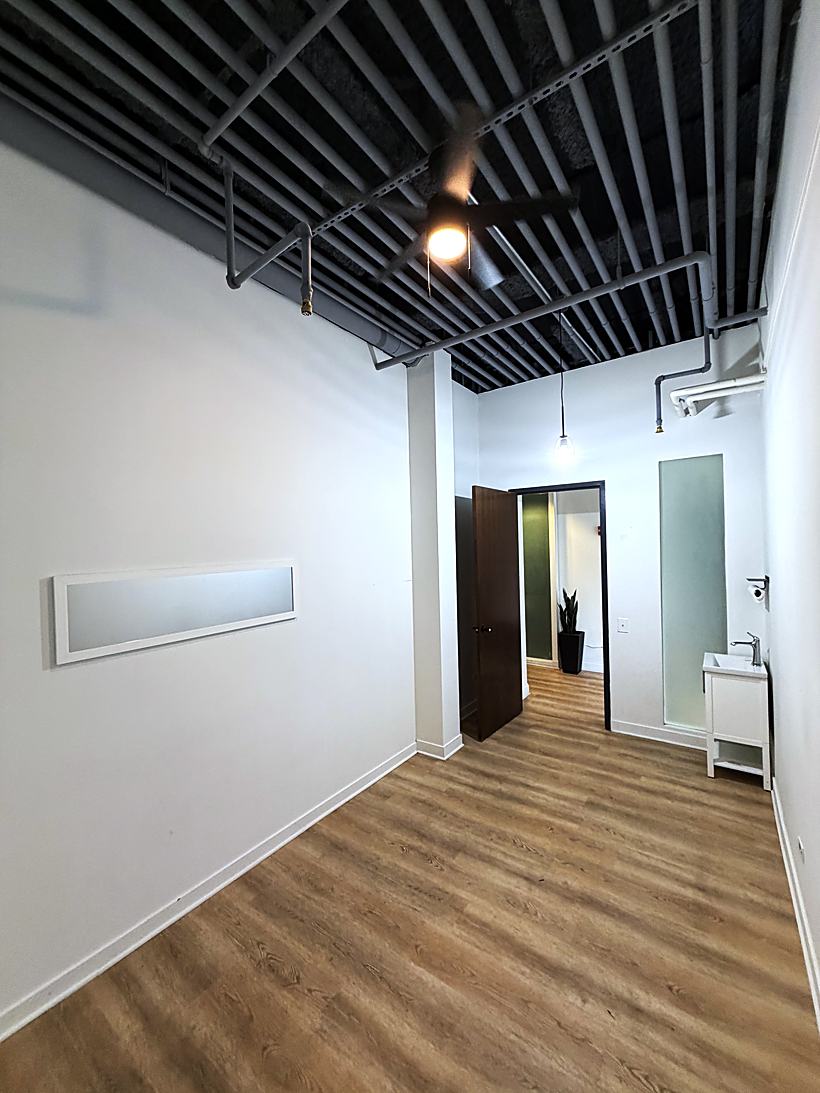 An open suite with exposed black ceiling, pipework, a sink and frosted glass panels