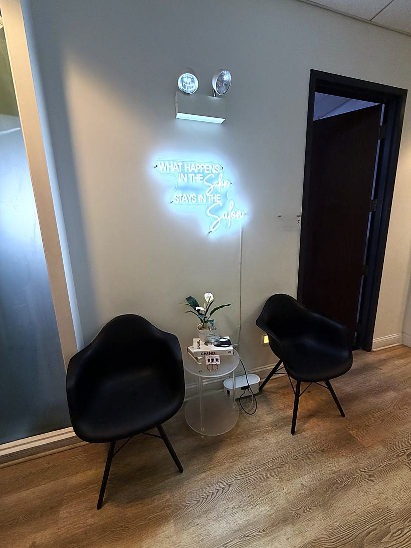 A seating nook with two black chairs under a neon sign reading what happens in the salon stays in the salon